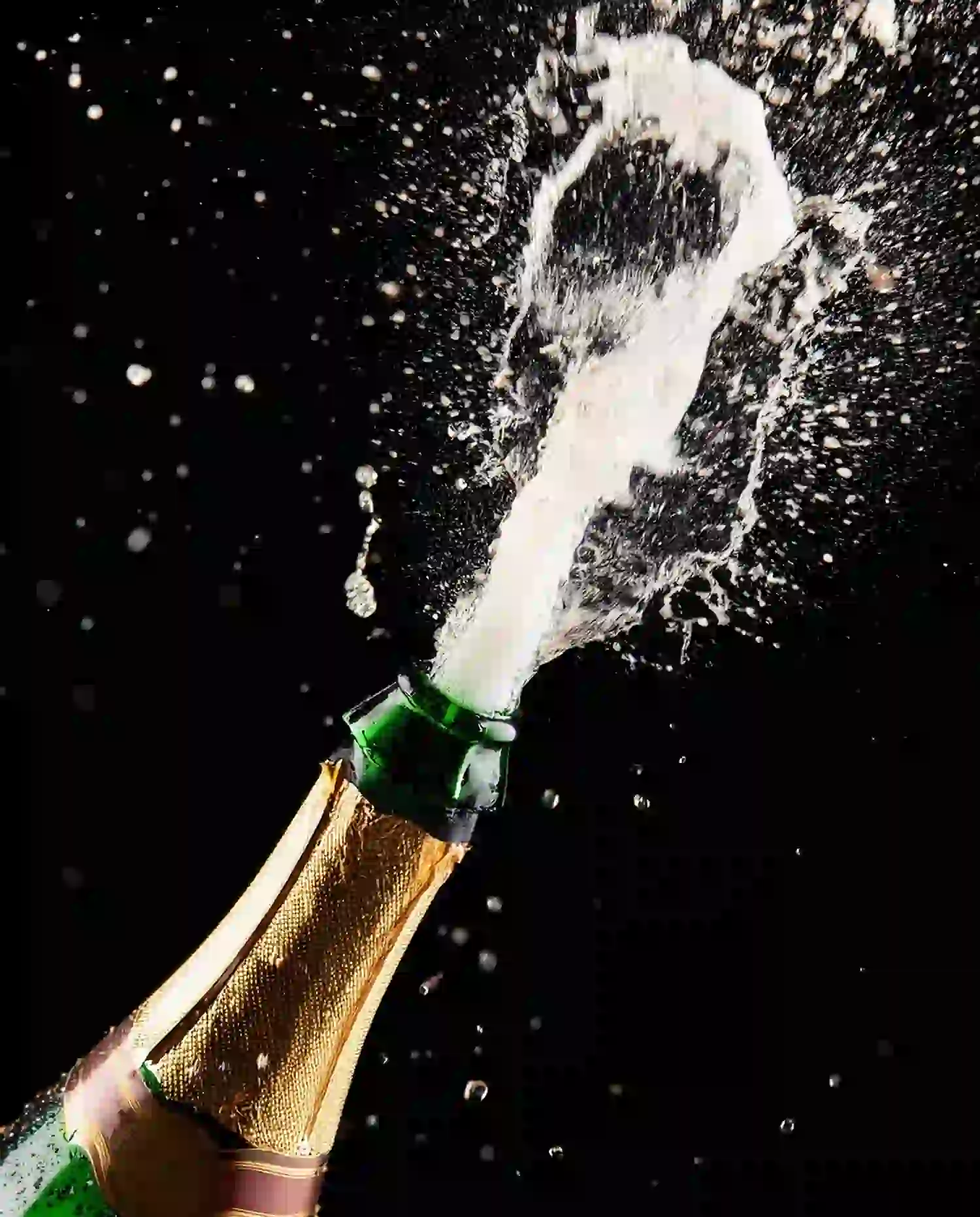 Eine Champagnerflasche wird geöffnet, der Korken fliegt heraus und ein Schwall Sekt spritzt vor schwarzem Hintergrund heraus – perfekt zum Feiern von Verwöhnpaketen und besonderen Momenten.